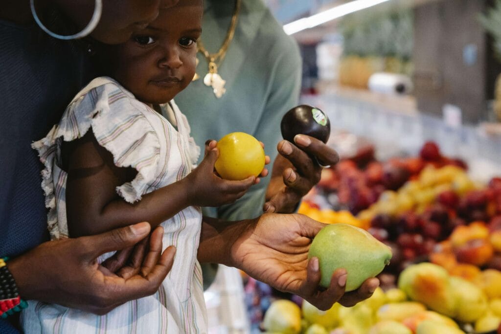 Criança com os pais escolhendo frutas para ilustrar o artigo sobre frutas seguras para bebês