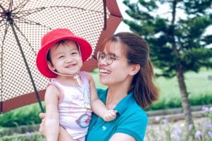 8 dicas sobre como cuidar do bebe no calor, mãe e filho passeando no parque usando chapéu e guarda sol